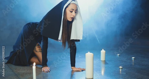 Attractive sexual nun sneaks up to a candle and blows out a candle in a dark smoky studio