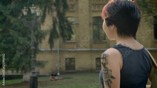 Extraordinary young women with tattooed hand walking away from university and holding skateboard photo