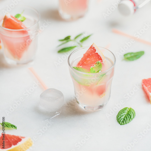 Flat-lay of cold refreshing summer alcohol cocktail with fresh grapefruit, mint leaves and ice over white marble background, selective focus, square crop