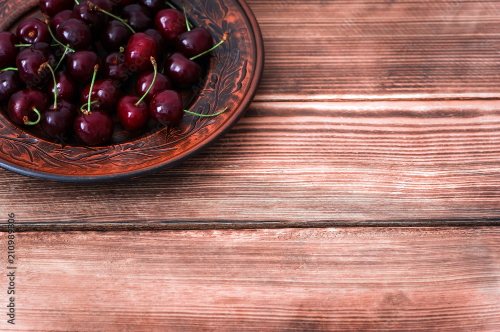 Fresh red cherries fruit on plate on wooden rustic background  with a copy space for text