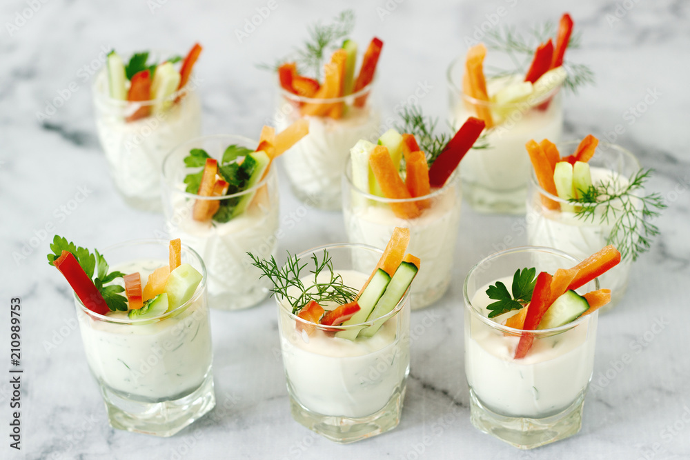 Snack in a glass with fresh cream and various vegetables on a light background.