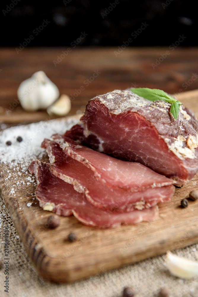 Pork dried meat slices on rustic dark wooden background. Dried pork prosciutto salami ham with herbs.