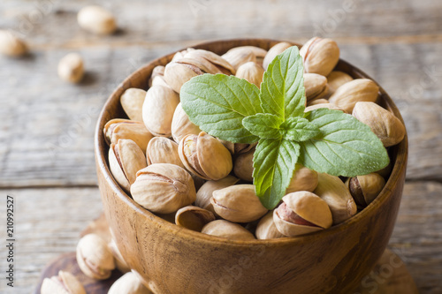 Delicious salted pistachios and fresh mint leaves on wooden background