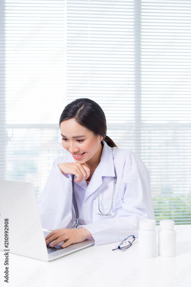 Young smiling female doctor sitting at office desk and working with a laptop Young smiling female doctor sitting at office desk and working with a laptop