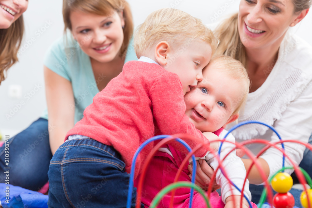 Group of happy young mothers watching their cute and healthy babies while playing with multicolored toys in a modern daycare center Group of happy young mothers watching their cute and healthy babies while playing with multicolored toys in a modern daycare center