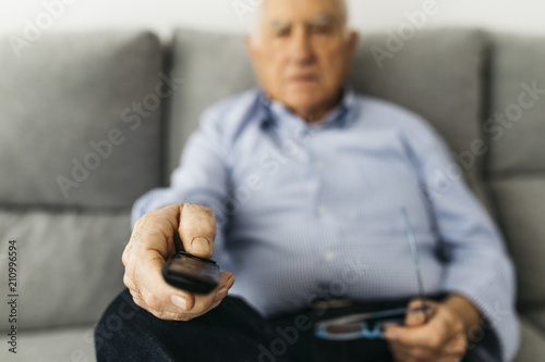 Senior man watching TV from the couch at home, focused on hand photo