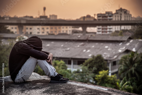 Young Asian man sitting on rooftop of abandoned building with depression stress out during sunset time in the city. Major depressive disorder concept