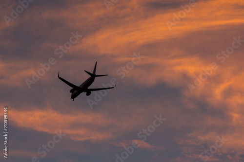 Landing airplane at urban colorful sunset. Silhouette, selective focus. Landscape, background.