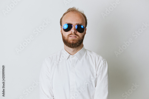 Serios fashionable young hipster bearded man wearing sunglasses and a white shirt.