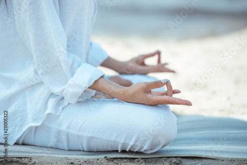 cropped image of woman in ardha padmasana (half lotus pose) on yoga mat by sea
