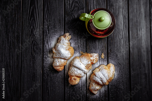 three croissants with tea on dark wooden background close-up top view