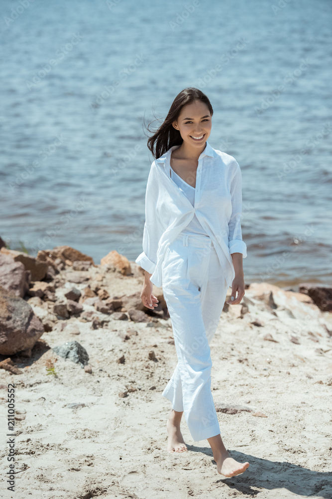 smiling asian woman walking on beach by sea during daytime