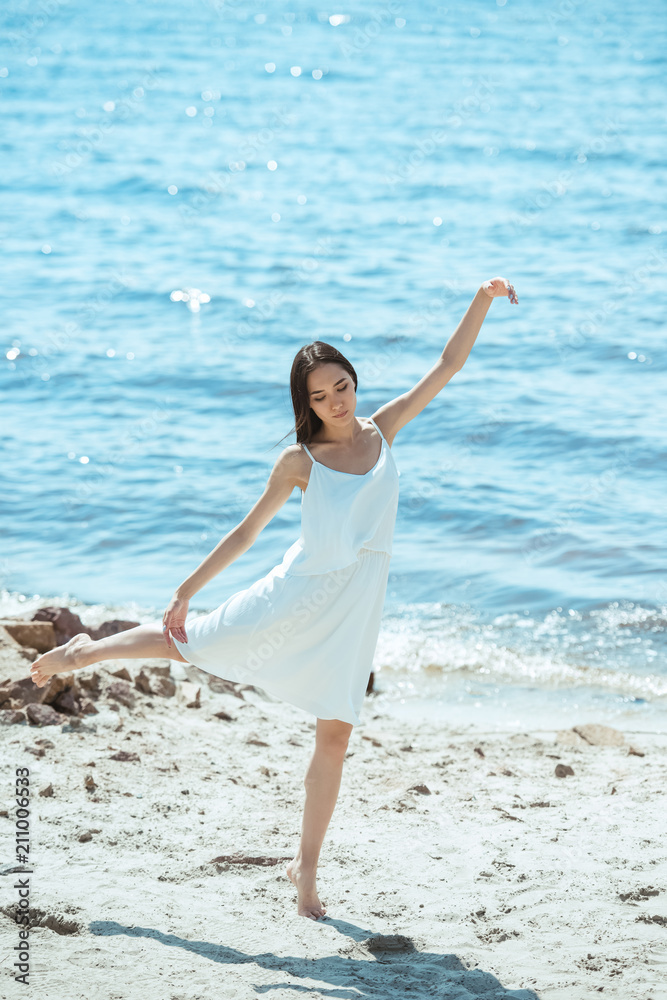 focused asian woman in white dress dancing on beach by sea