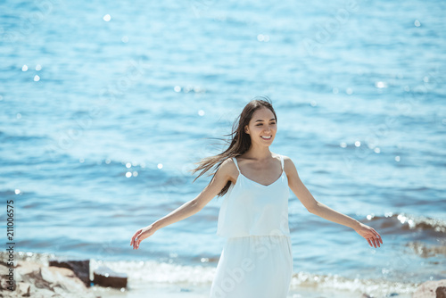 happy asian woman in white dress with wide arms standing by sea