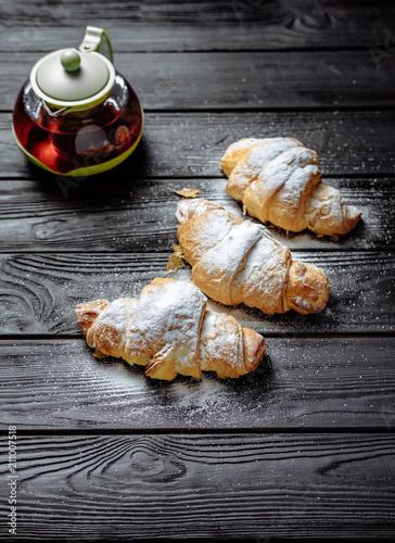 three croissants with tea on dark wooden background close-up top view