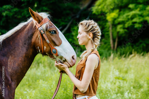 Beautiful blond two braids young woman with a horse face to face outdoor, side view, green background.