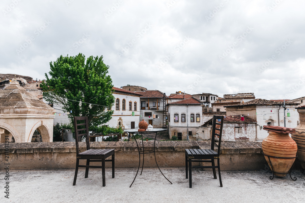 round table and wooden chairs on terrace and historical houses behind in cappadocia, turkey