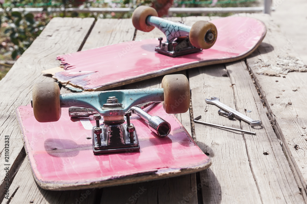 The old broken skateboard lies with a spanner on a wooden table in the open air. Toned