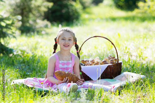 A child is eating bread sitting on the grass. A little girl bites bread from her hands in the summer on a picnic in a city park.