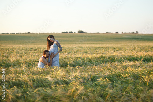 Счастливый молодой мужчина и счастливая, молодая, беременная женщина на закате в пшеничном поле