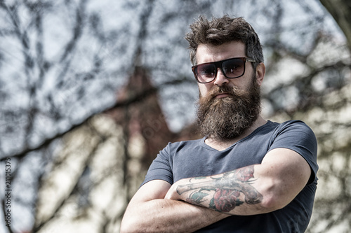 Man with beard and mustache on strict face, nature background, defocused. Bearded man wears stylish sunglasses. Hipster with beard looks stylish and confident on sunny day. Fashion and style concept