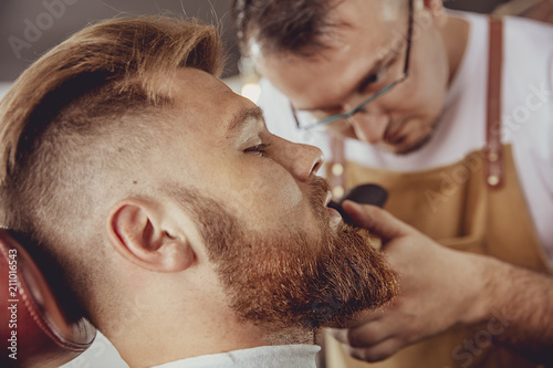 Man in the process of trimming a beard in a barbershop. Photo in vintage style