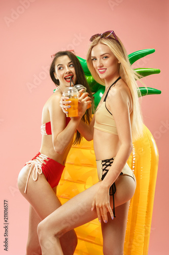 Cute girls in swimsuits posing at studio. Summer portrait caucasian teenagers on pink background.