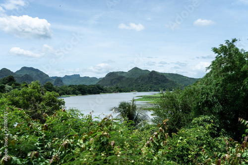 View of river Kwai with mountains and tropical forest and in background and trees in the foreground during a bright sunny day, Kanchanaburi, Thailand