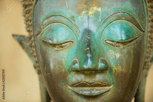 Close up of a face of an ancient copper Buddha statue outside of the Hor Phra Keo temple (former temple of the Emerald Buddha) in Vientiane, Laos.