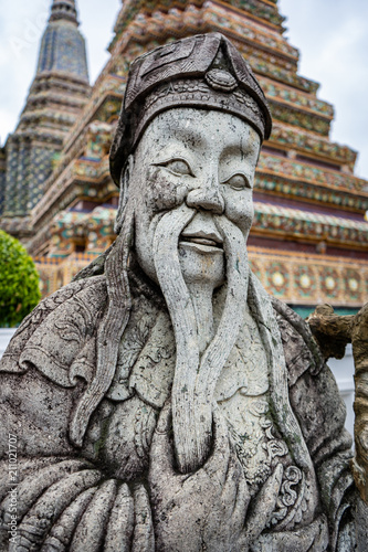 Traditional Thai stone buddha sculpture with pagone in the background in a Thai temple, Wat Pho, Bangkok, Thailand