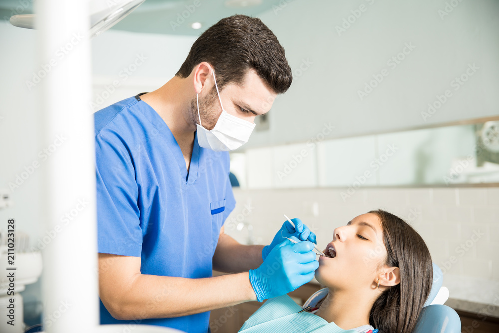 Dentist Examining Teenage Girl With Dental Tools At Clinic Dentist Examining Teenage Girl With Dental Tools At Clinic