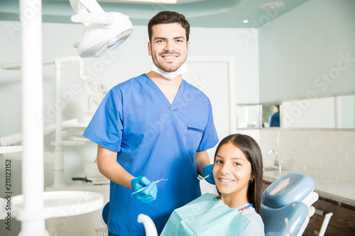 Portrait Of Smiling Male Dentist And Teenage Girl At Clinic
