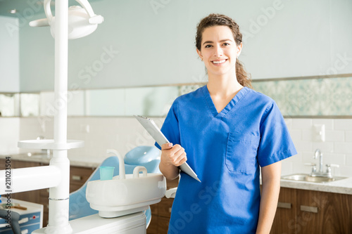 Portrait Of Smiling Dentist With Clipboard Standing At Clinic