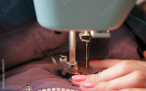 Fototapeta Naklejka Na Ścianę i Meble -  Close-up of seamstresses's hands sews to blue jacket leather inserts on sewing mashine. Side view.