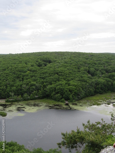 View over the edge of a cliff on a mountain on Lantern Hill trail in Connecticut  with a pond below in the distance 