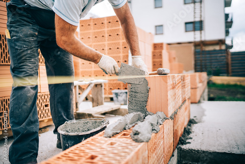 Foto Close up of industrial worker, bricklayer installing bricks on construction site