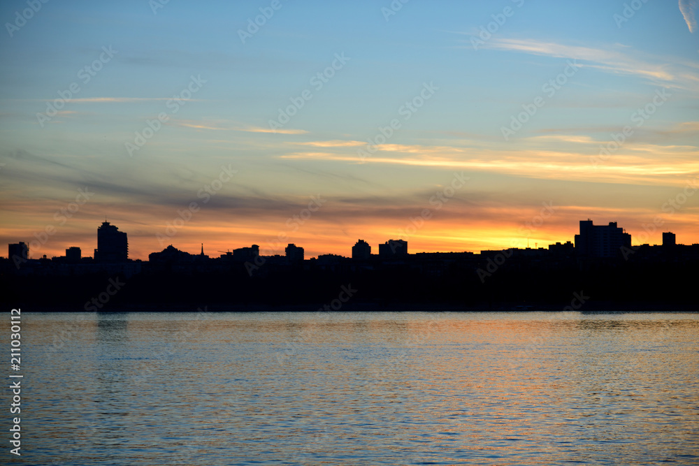 Silhouette of the city by the river at sunset.