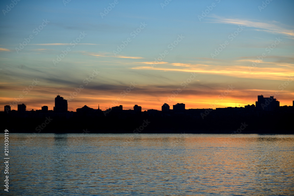 The embankment of the city of Volgograd during sunset. The silhouette of the city on the river during sunset, clear sky, a little feather clouds during sunset over the horizon.