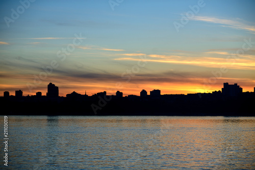 The embankment of the city of Volgograd during sunset. The silhouette of the city on the river during sunset, clear sky, a little feather clouds during sunset over the horizon. © makalish