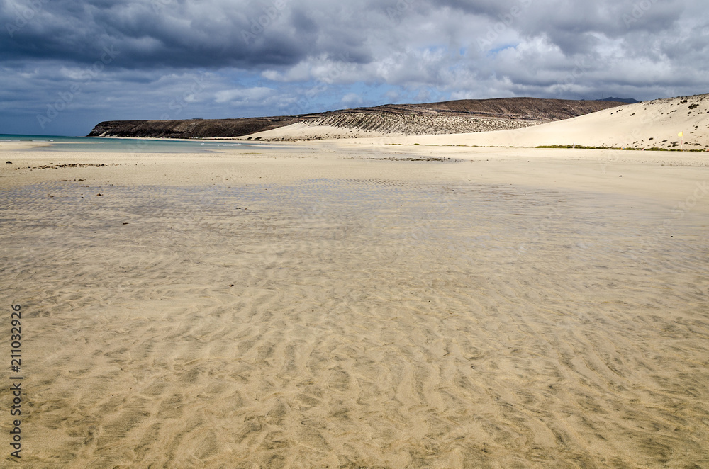 Low tide on Sotavento beach on Fuerteventura, Canary Islands with stormy dramatic sky and water trails in the sand Low tide on Sotavento beach on Fuerteventura, Canary Islands with stormy dramatic sky and water trails in the sand