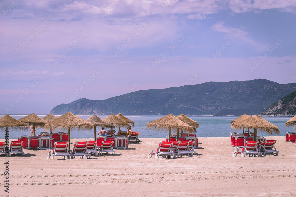 Straw umbrellas and chairs at a sandy beach in Troia, Portugal