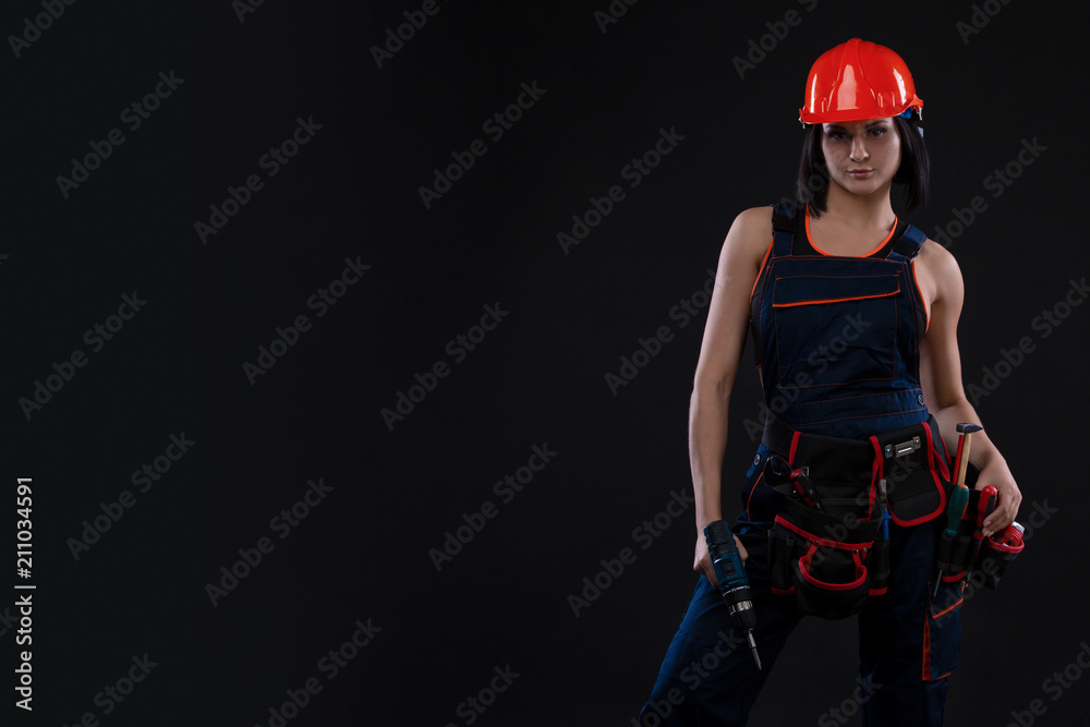 Attractive young woman doing repairs at black background. Portrait of a female construction worker. Building, repair concept. Copy space Attractive young woman doing repairs at black background. Portrait of a female construction worker. Building, repair concept. Copy space