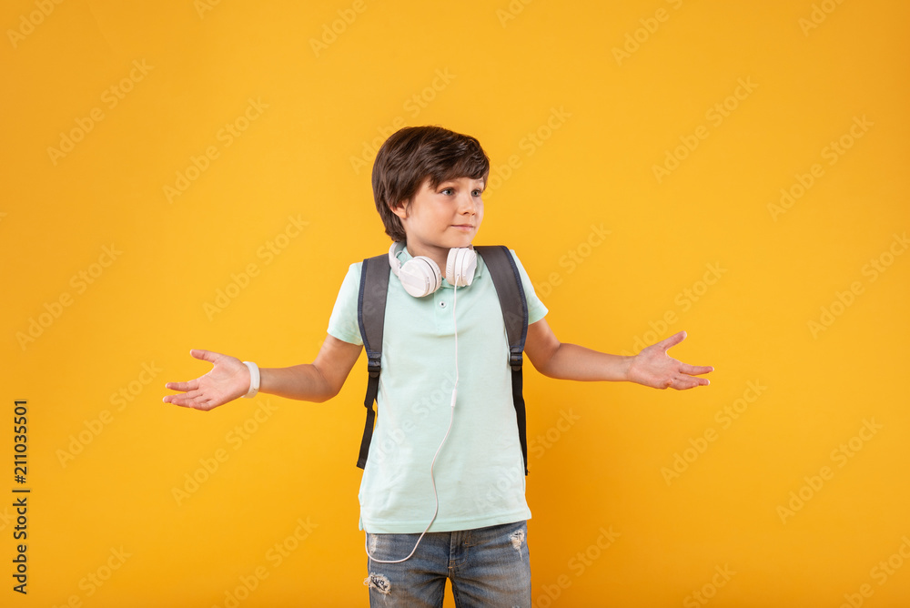 No idea. Baffled dark-haired boy wearing headphones and a schoolbag and thinking No idea. Baffled dark-haired boy wearing headphones and a schoolbag and thinking