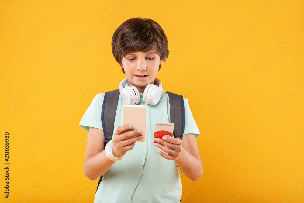 Wonderful device. Happy dark-haired boy smiling and holding his advanced phone Wonderful device. Happy dark-haired boy smiling and holding his advanced phone