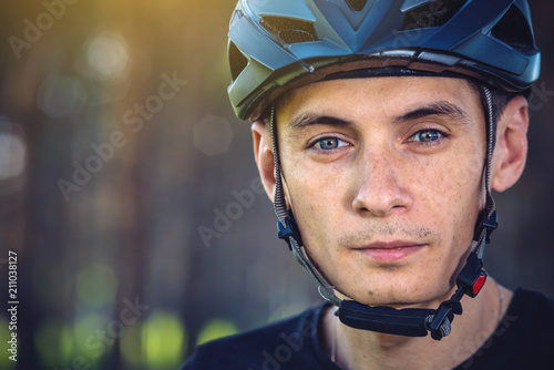 Man cyclist is wearing a sports gray helmet on his head in the background of green nature.