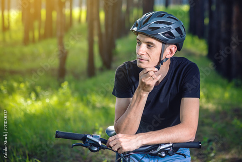 Fototapeta Naklejka Na Ścianę i Meble -  Cyclist is wearing a sports helmet on his head in the background of green nature. Concept of protection during Cycling