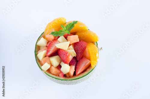 Melon stuffed with assorted fruits on white background. Flat lay.