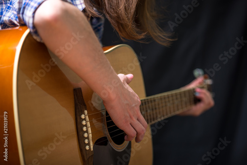Girl playing an acoustic guitar on a dark background in the Studio. Concert young musicians