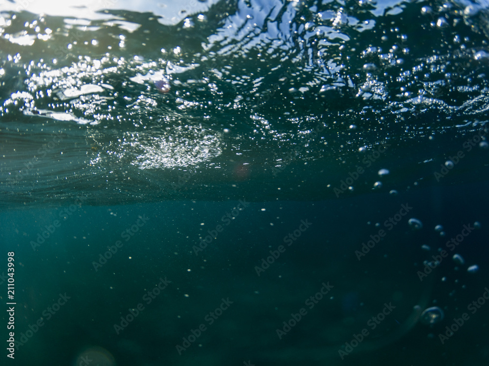 Sea water wave with bubbles closeup underwater photo. Blue sea surface from below. Ripples on sea surface. Sea water wave with bubbles closeup underwater photo. Blue sea surface from below. Ripples on sea surface.