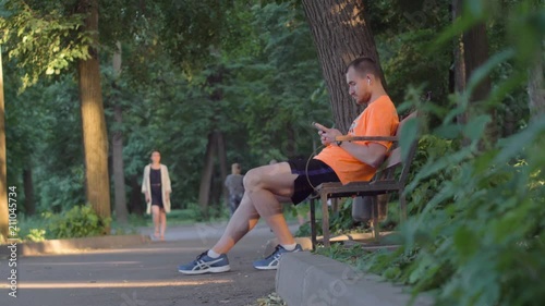 Man with phone and wireless headphones on a bench photo